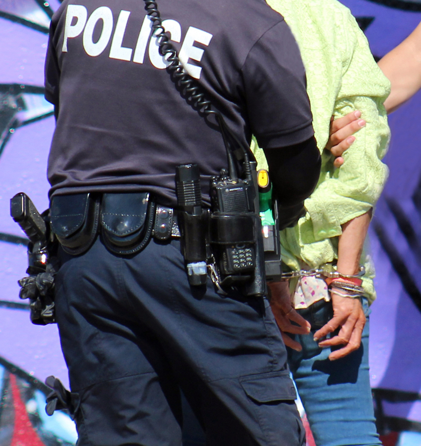 Police officer arrests a person. No one's face is visible, and the person being arrested has handcuffs on.