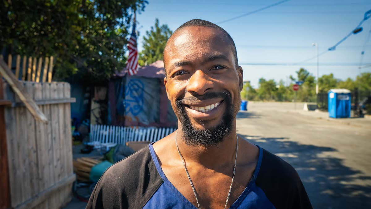 Man smiling outside a homeless encampment.