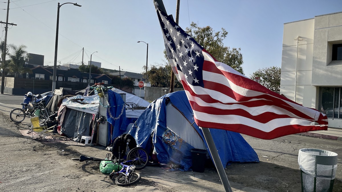 An American flag can be seen next to a tent in a homeless encampment.