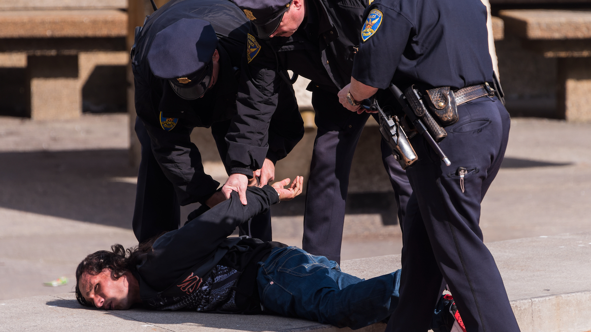 Homeless man on the ground, being arrested by multiple officers.