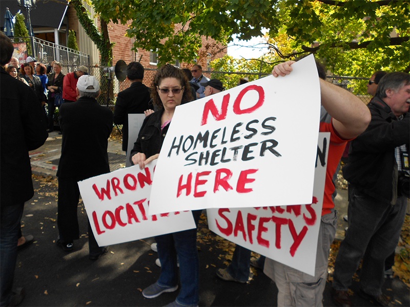 A group of protestors hold signs opposing a homeless shelter in their neighborhood.