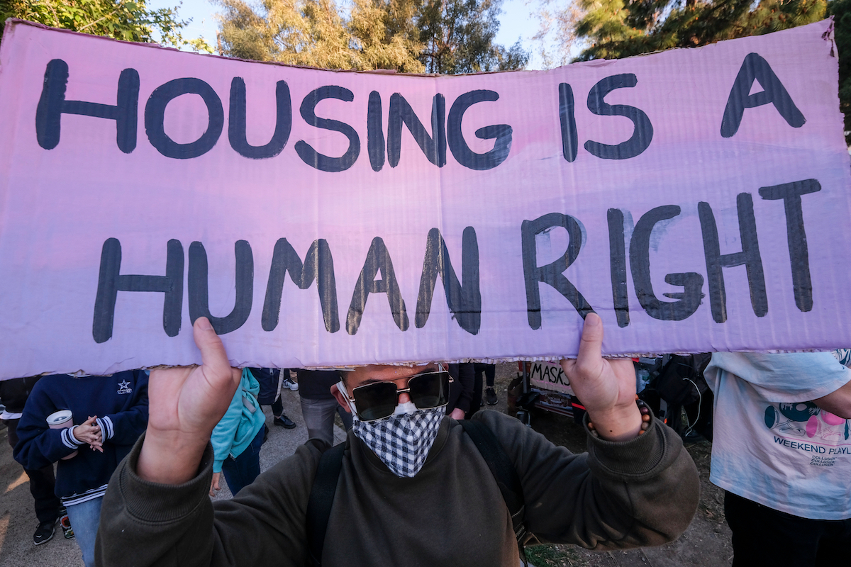 A person holds a sign reading 'Housing is a Human Right'.