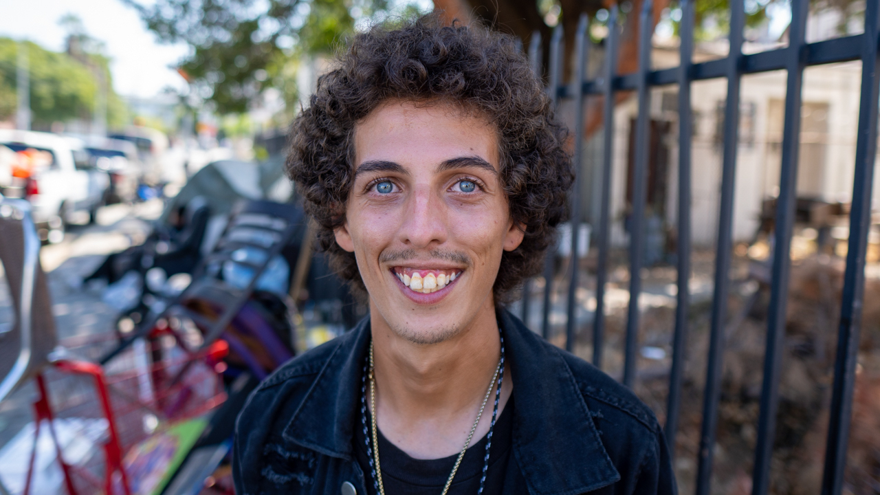 Portrait of young homeless man standing outside.