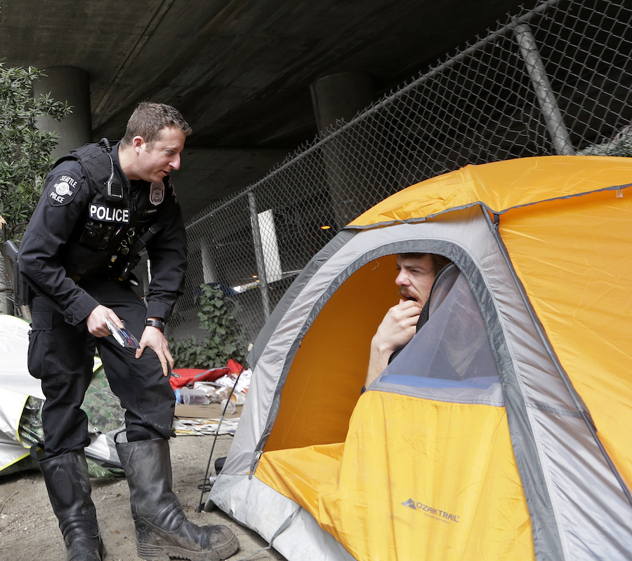 Police officer talks to a homeless man who is peeking out of his tent.