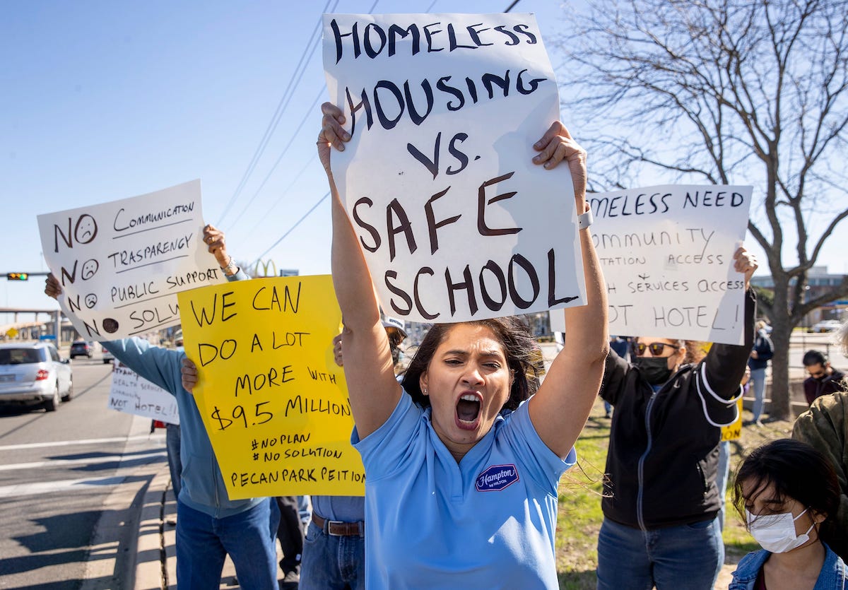 A group of hotel workers protests the use of hotel rooms for homeless people. One woman in front has a sign that reads 'Homeless Housing vs. Safe School'.