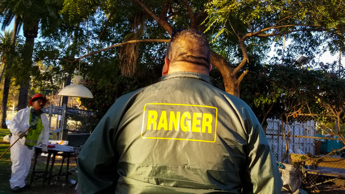 park ranger watches as sanitation workers throw out a homeless person belongings in Echo Park Lake