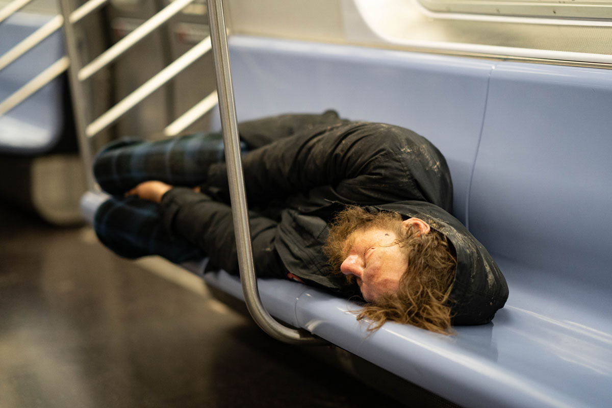 a homeless man sleeps on a NYC subway bench during Coronavirus