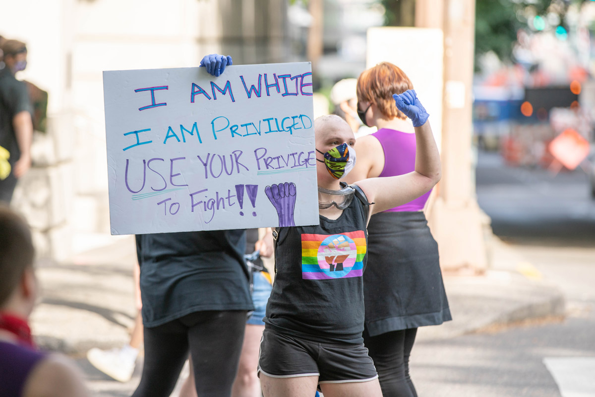 White protester holds sign telling white people to use their privilege to help people of color