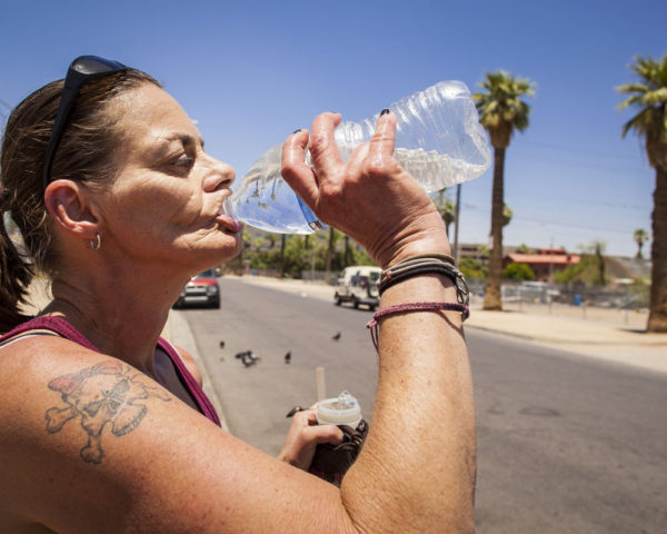 homeless woman drinks from a bottle of water in Phoenix, AZ