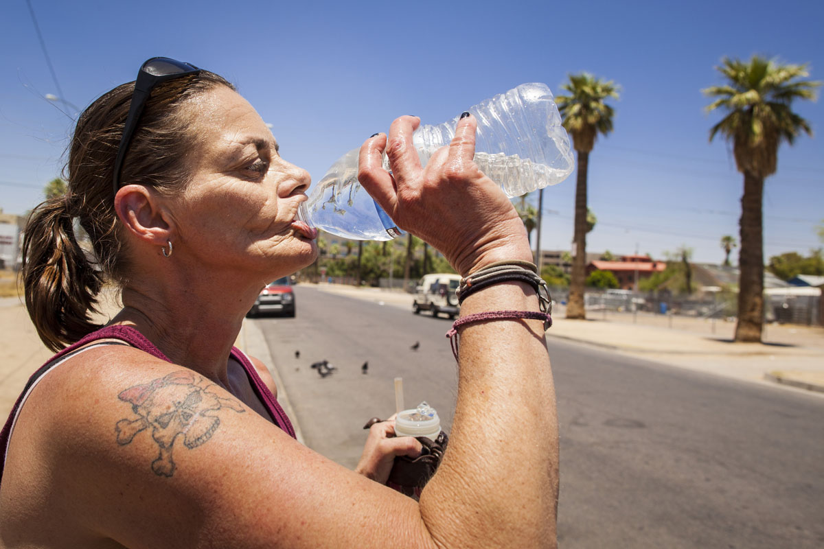 homeless woman drinks from a bottle of water in Phoenix, AZ