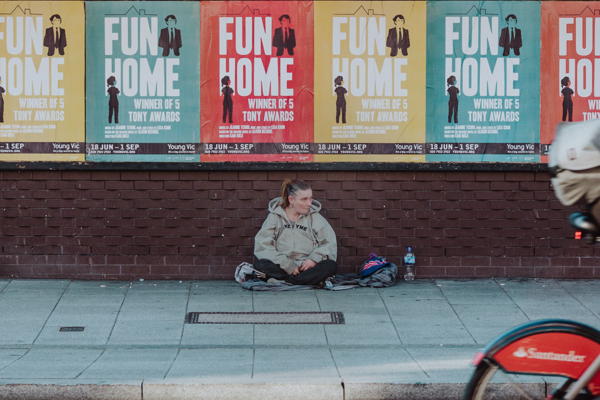 homeless woman sits on a sidewalk in London